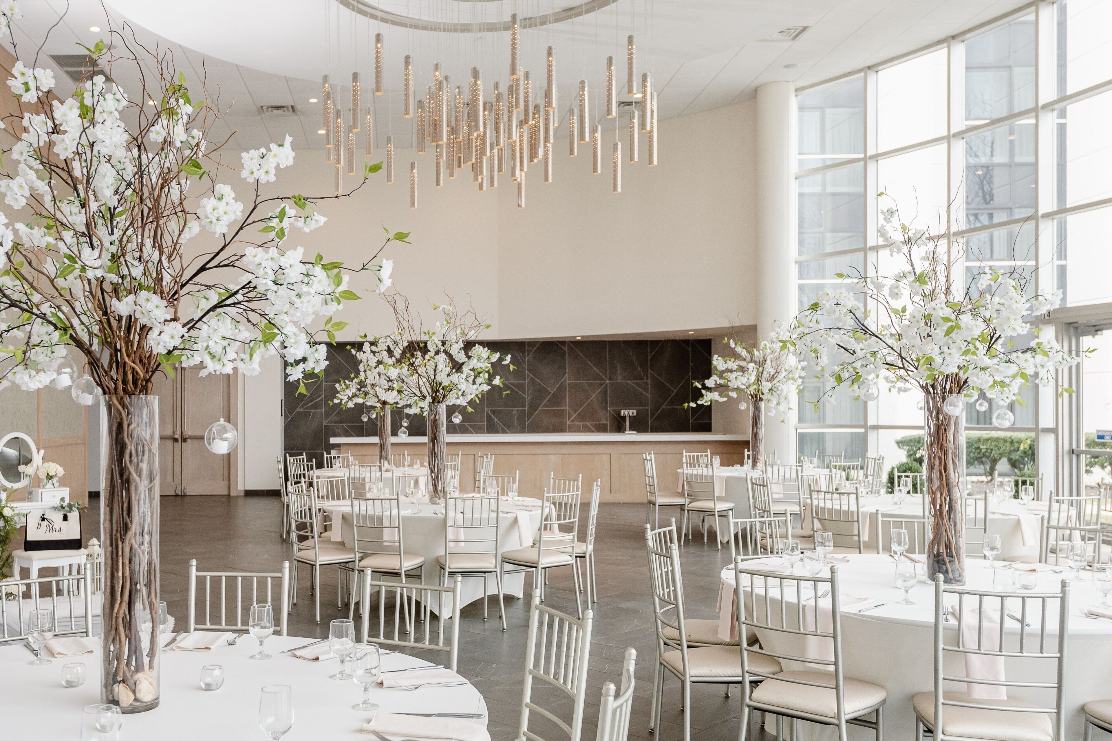 Un vaste espace dédié à la salle à manger, avec des tables rondes, des chaises blanches et des centres de table ornés de motifs floraux.