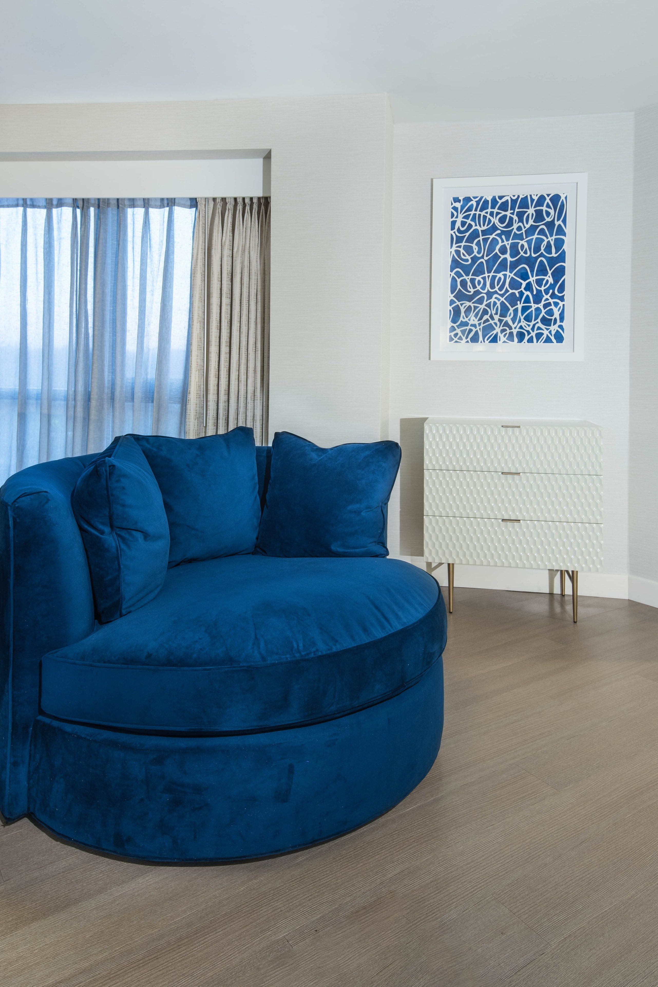 A modern living room with a blue sectional sofa, a white cabinet, and a framed abstract artwork on the wall.