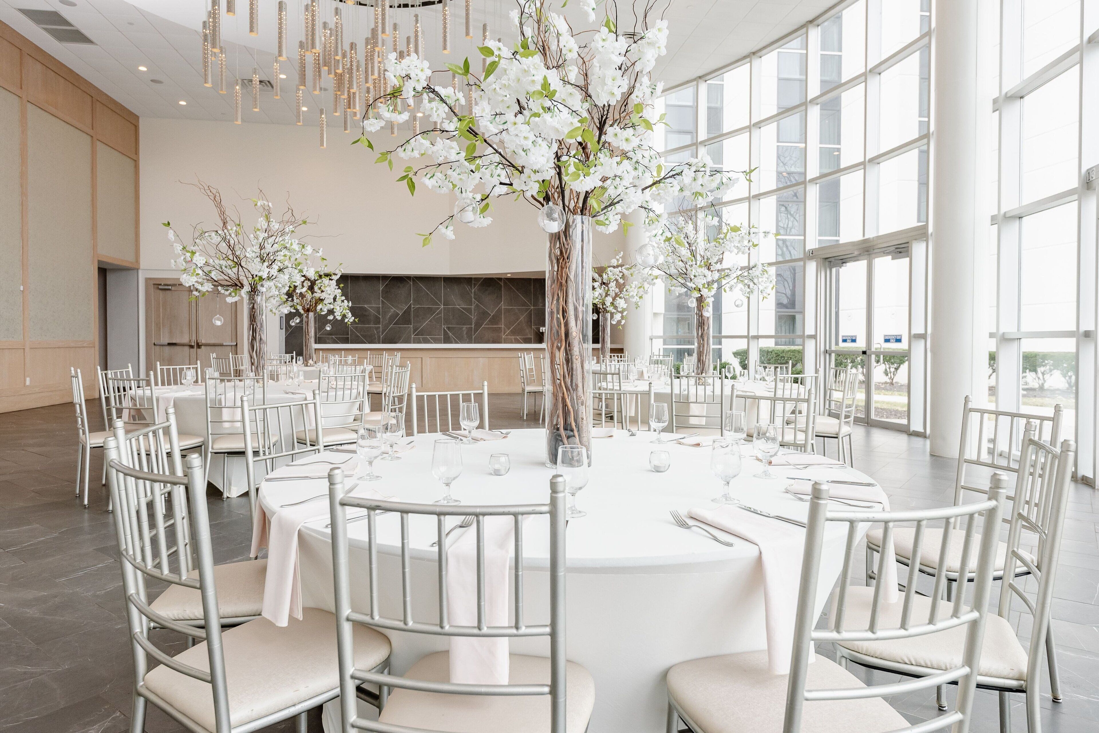 A spacious banquet hall with round tables, white chairs, and floral centerpieces.