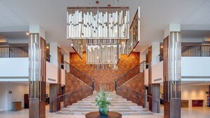 Un hall espacioso con una escalera central, una lámpara de araña moderna y un mostrador de recepción.