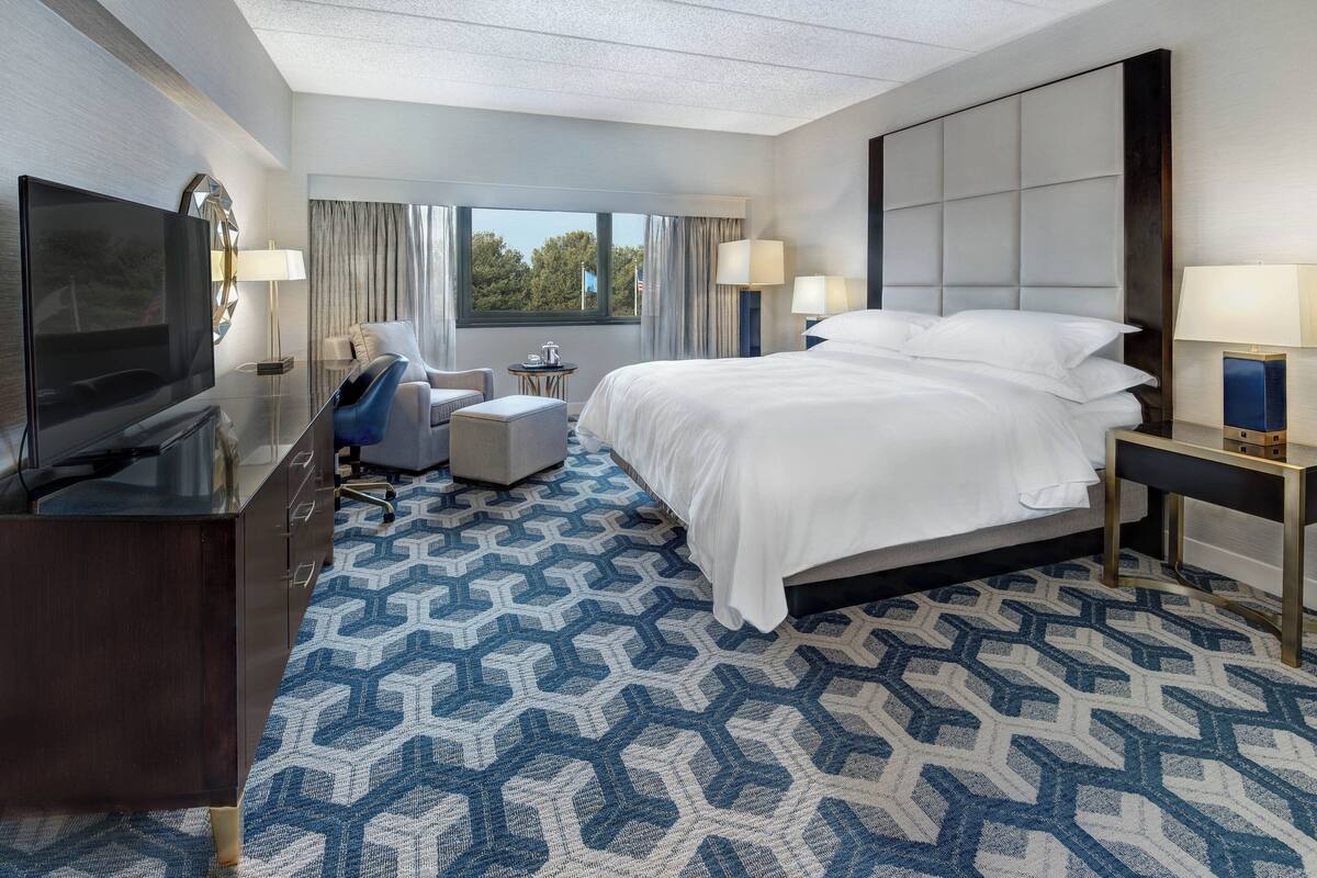 A hotel room with a large bed, a TV, a desk, and a chair.
