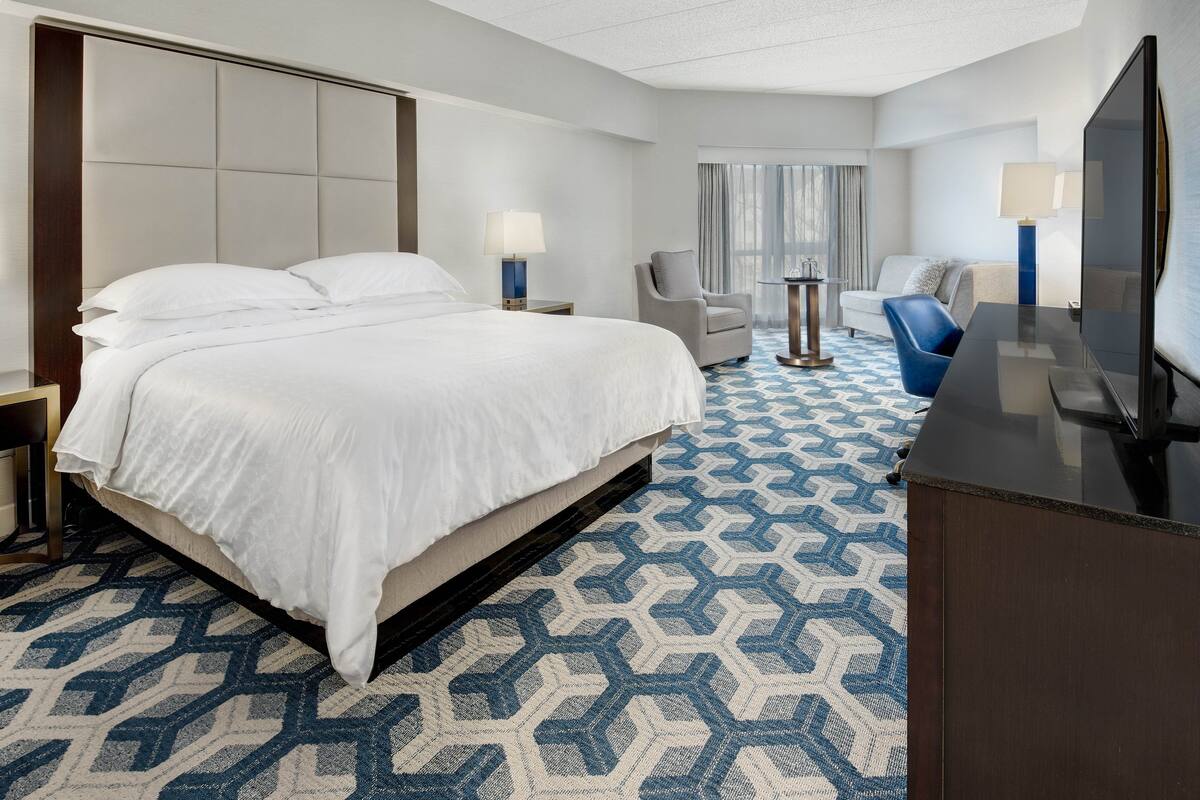 A hotel room with a large bed, a desk, a chair, and a TV.