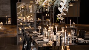 Una larga mesa de comedor dispuesta con velas, cristalería y un centro de mesa floral.