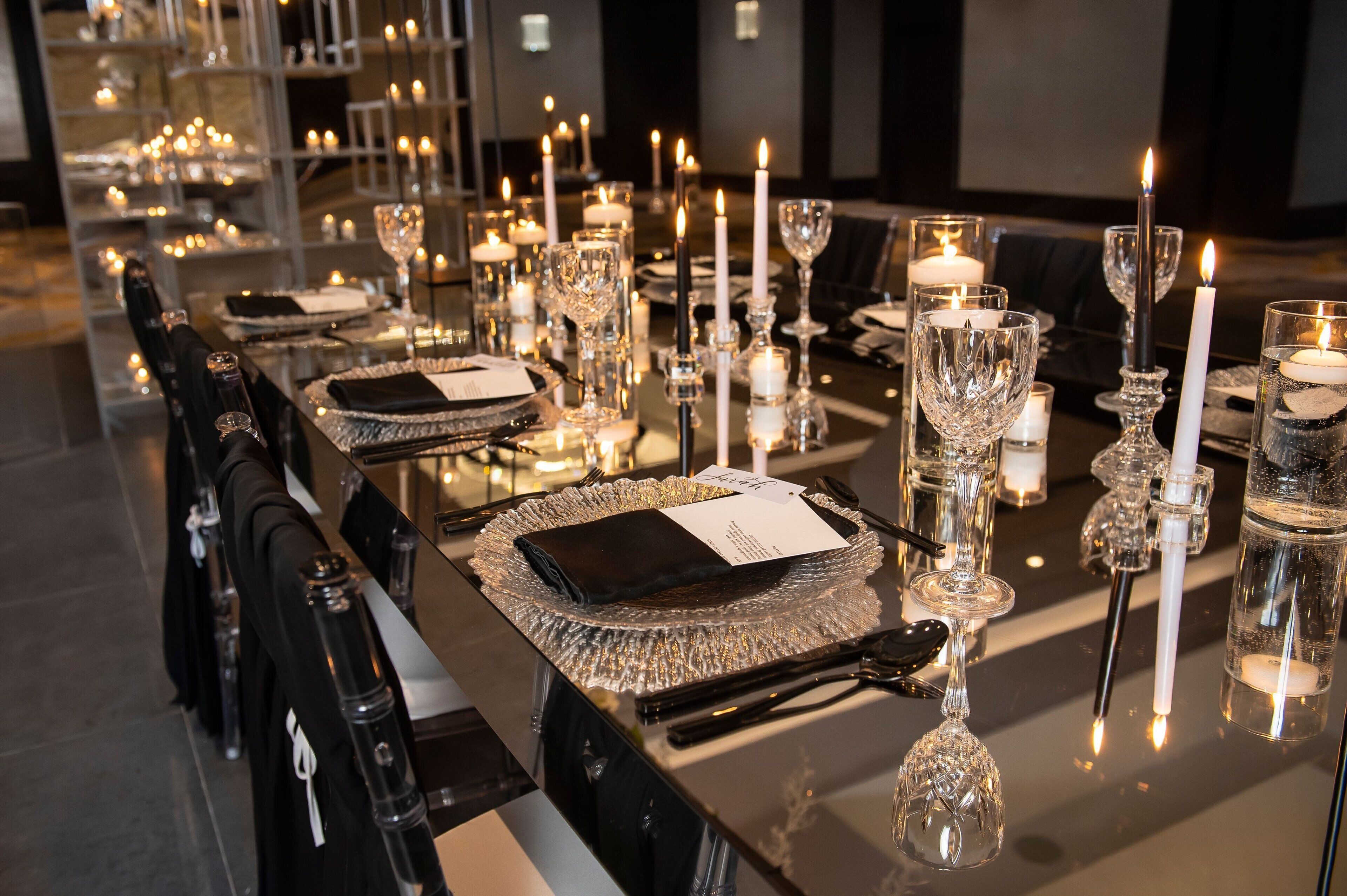 A long dining table set with clear glassware, candles, and black napkins.