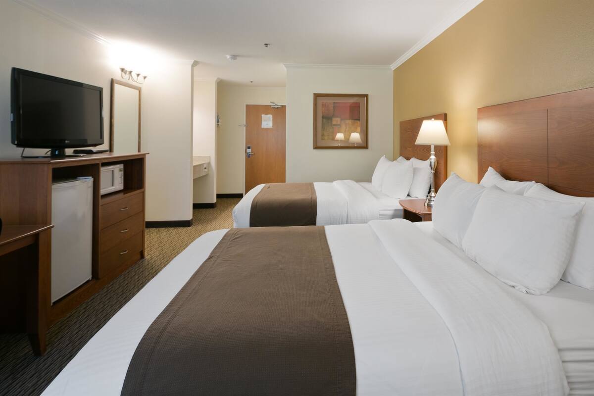 A hotel room with two beds, a television, a desk with a computer, and a door.