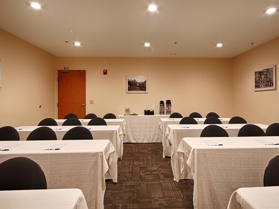 A conference room with rows of tables and chairs, a door, and two framed pictures on the walls.