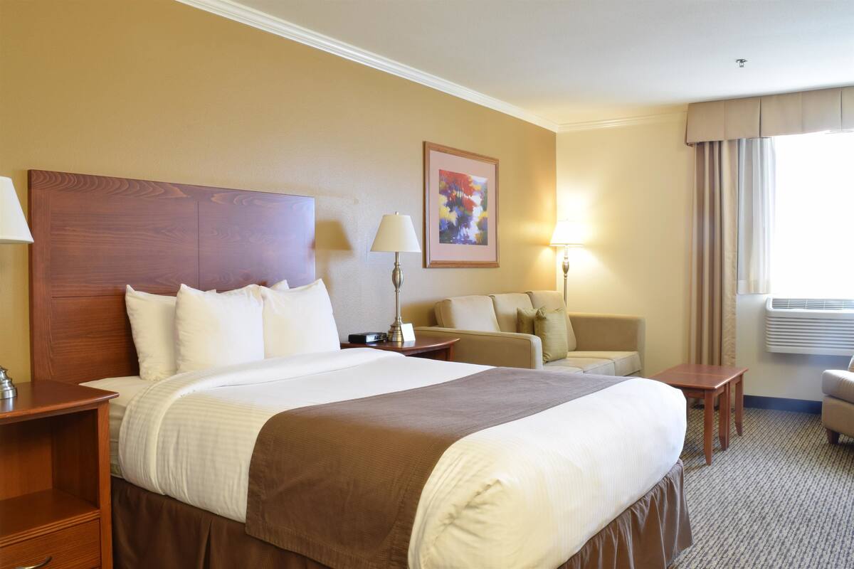 A hotel room with a large bed, a sofa, a desk, and a window with curtains.