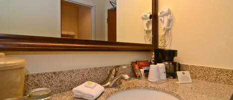 A hotel bathroom with a granite countertop, a white sink, a towel, a coffee maker, and a hairdryer on the wall.