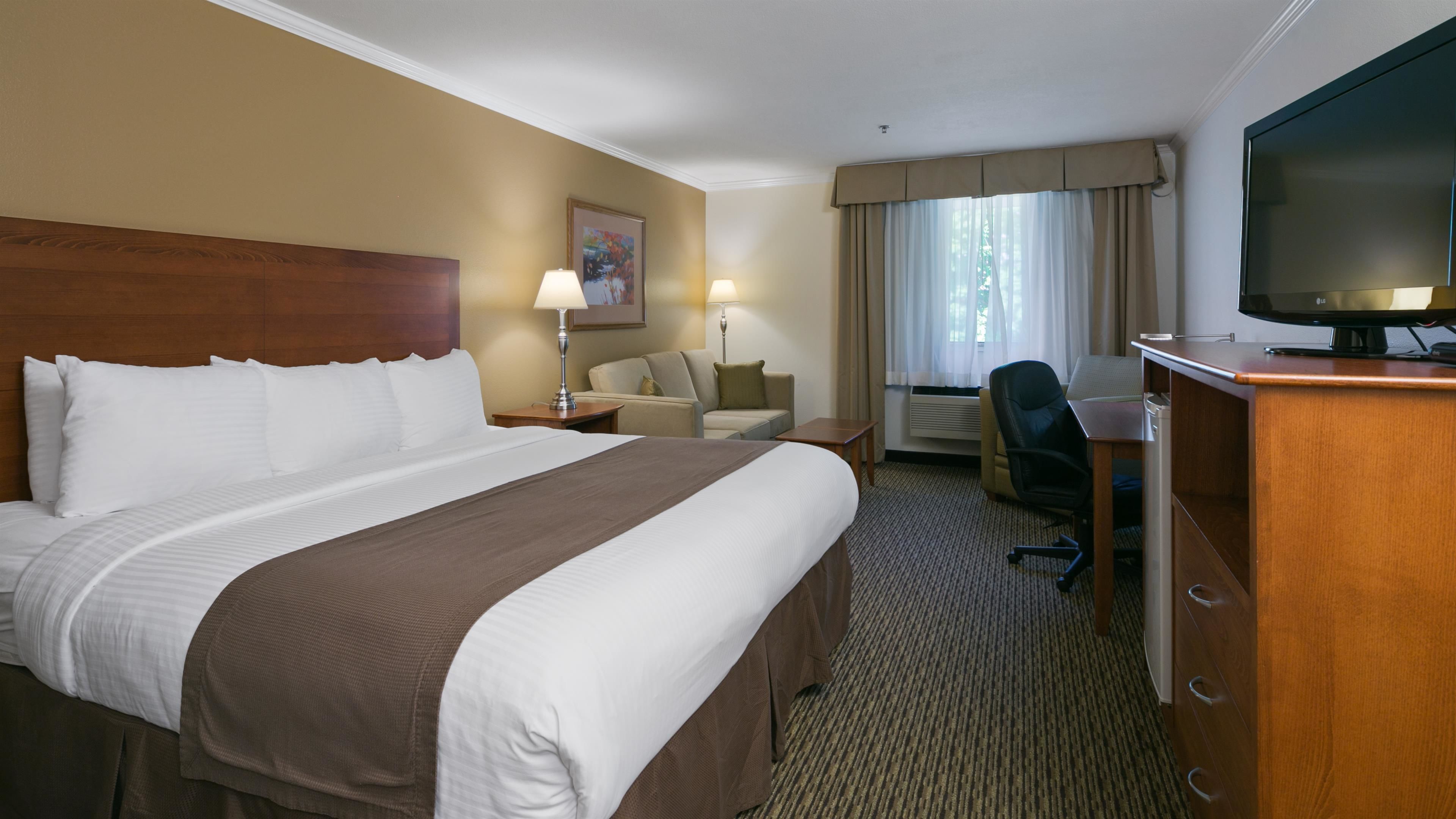 A hotel room with a large bed, a desk with a chair, a television, and a window with curtains.