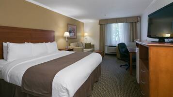 A hotel room with a large bed, a desk with a chair, a television, and a window with curtains.
