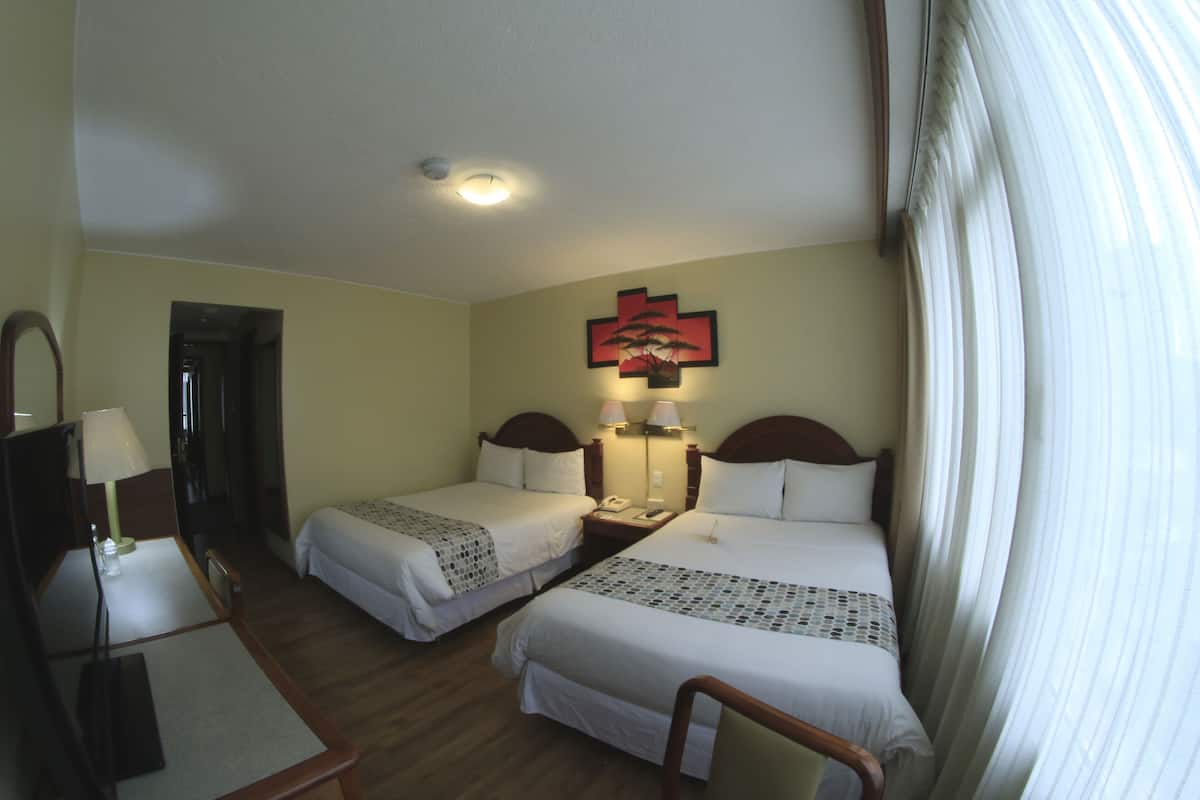 Une chambre d’hôtel avec deux lits, un bureau, une chaise, un miroir et une lampe fixée au mur.