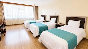 A hotel room with three beds, a desk, and a large window with curtains.