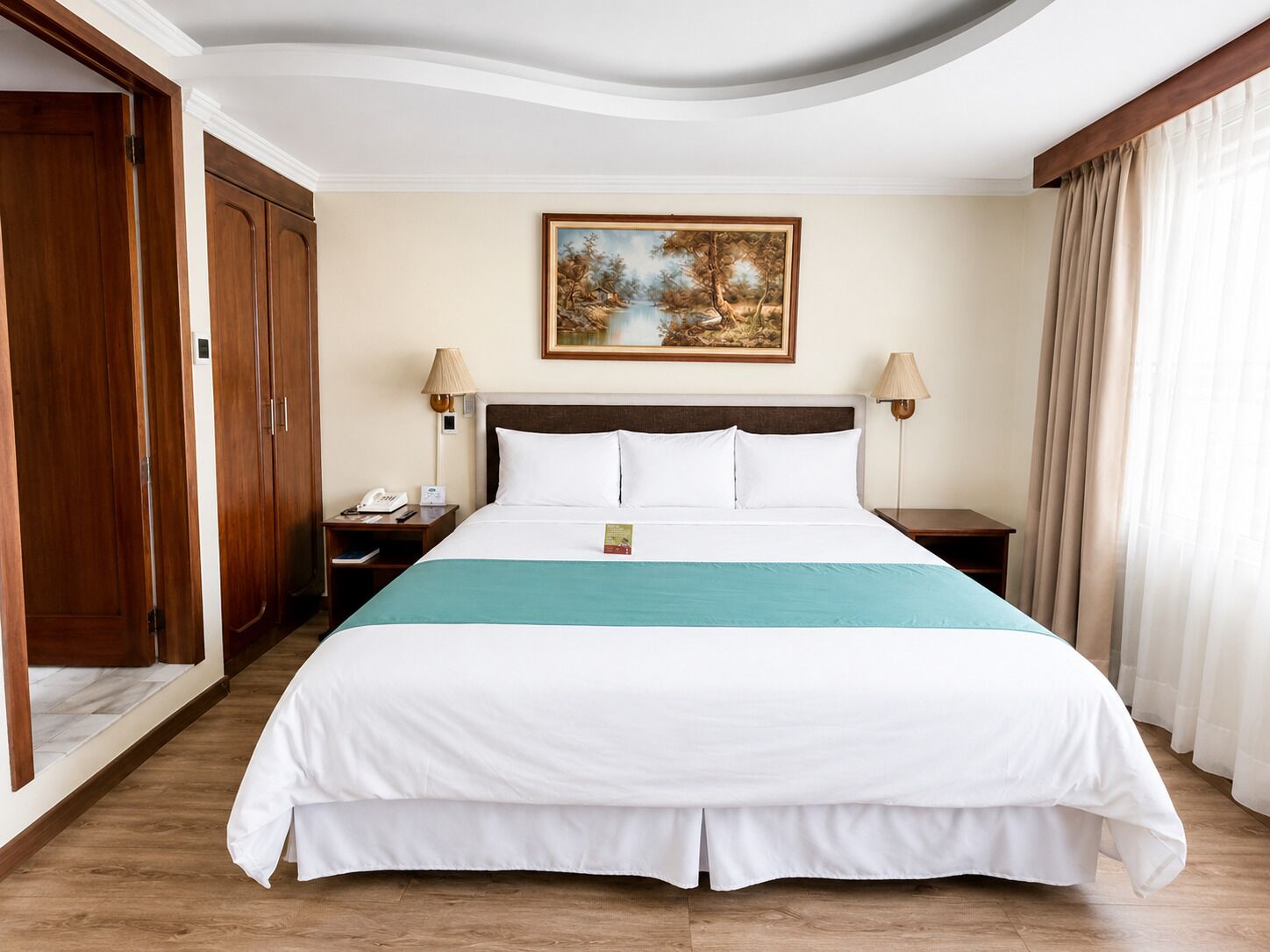 A hotel room with a large bed, wooden wardrobe, a painting on the wall, and a view of the outdoors.