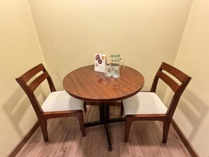 Pyöreä puinen pöytä, jossa on kaksi tuolia, lasinen kannu ja ruokalista.