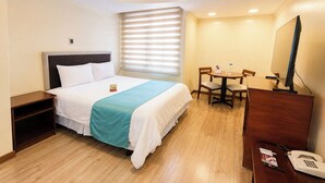 Habitación de hotel con cama, escritorio con computadora, teléfono y ventana con persianas.