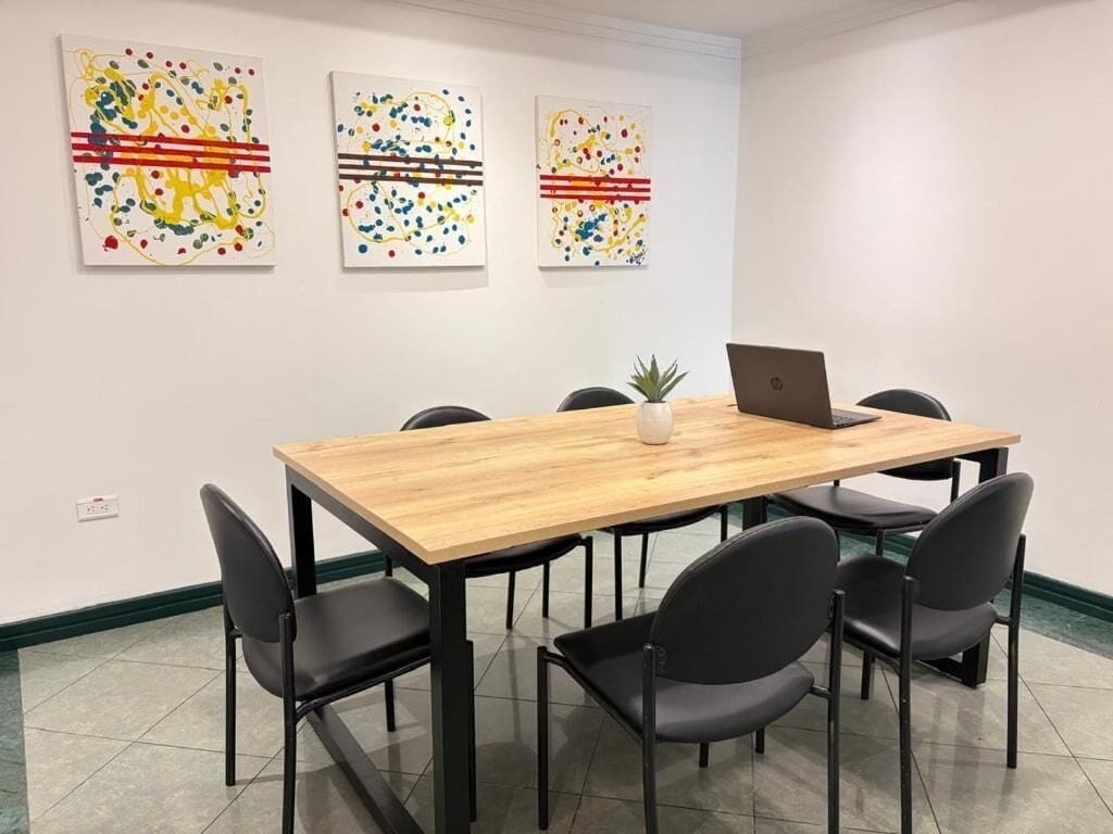 Une salle de conférence avec une table en bois, six chaises noires et trois tableaux abstraits accrochés au mur.