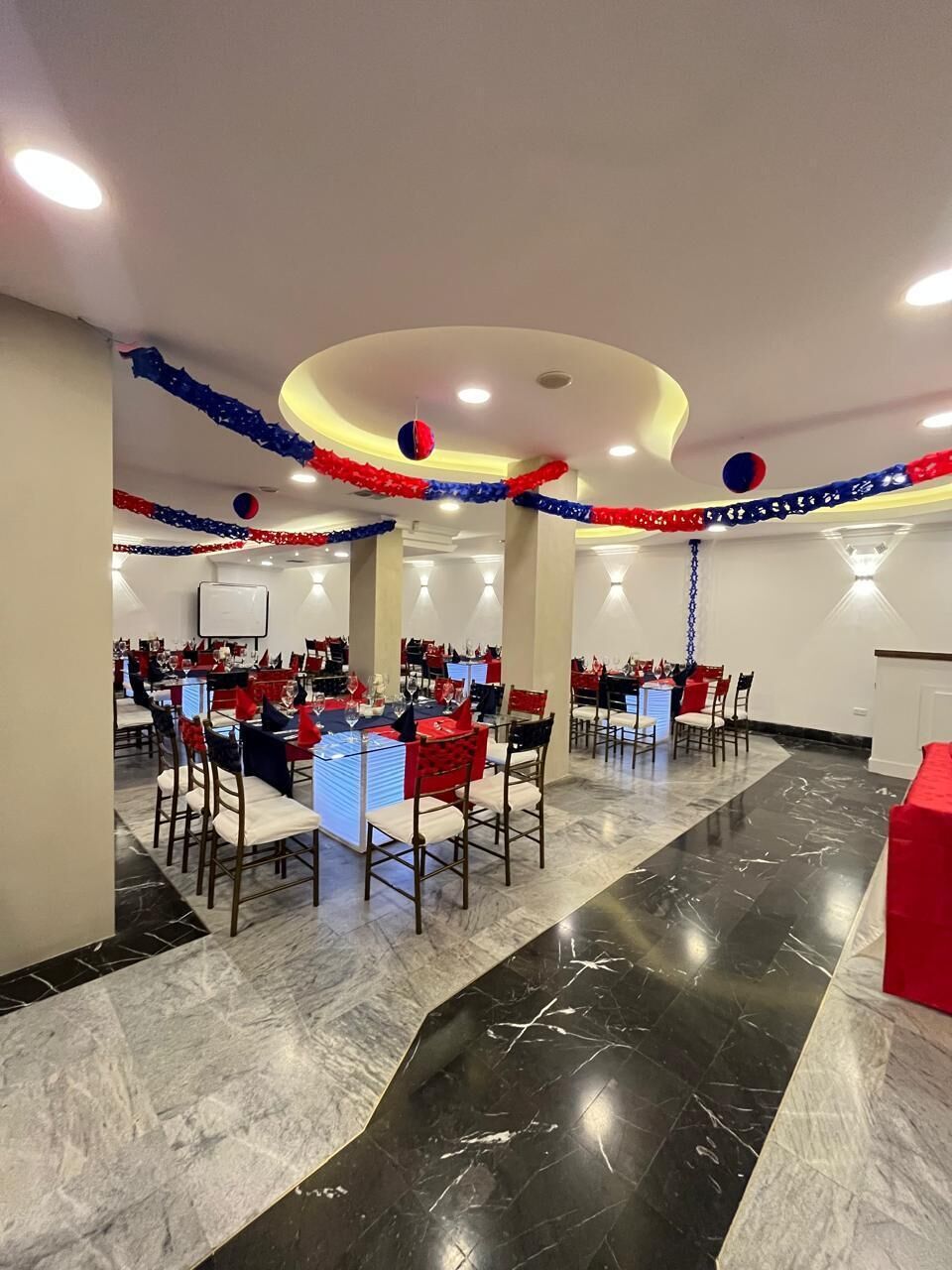 A conference room with multiple tables and chairs, a whiteboard, and red and blue decorations on the ceiling.