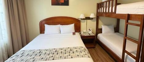 A hotel room with a large bed, a bunk bed, a bedside table with a lamp, and a wall-mounted painting.
