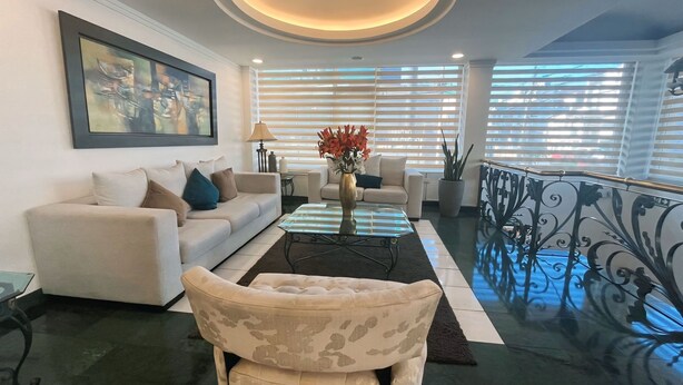 Uma sala de estar com sofá, poltronas, mesa de centro e um vaso decorativo.