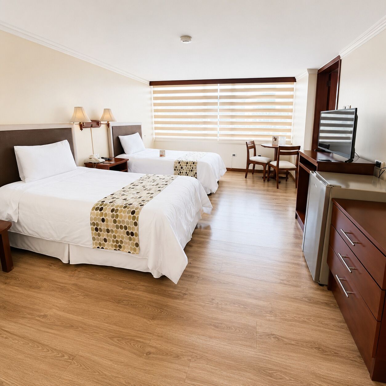 A hotel room with two beds, a desk, a chair, a television, and a refrigerator.
