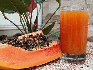 A glass of orange juice and a half-cut papaya with black seeds on a table. - Hotel República (Quito)