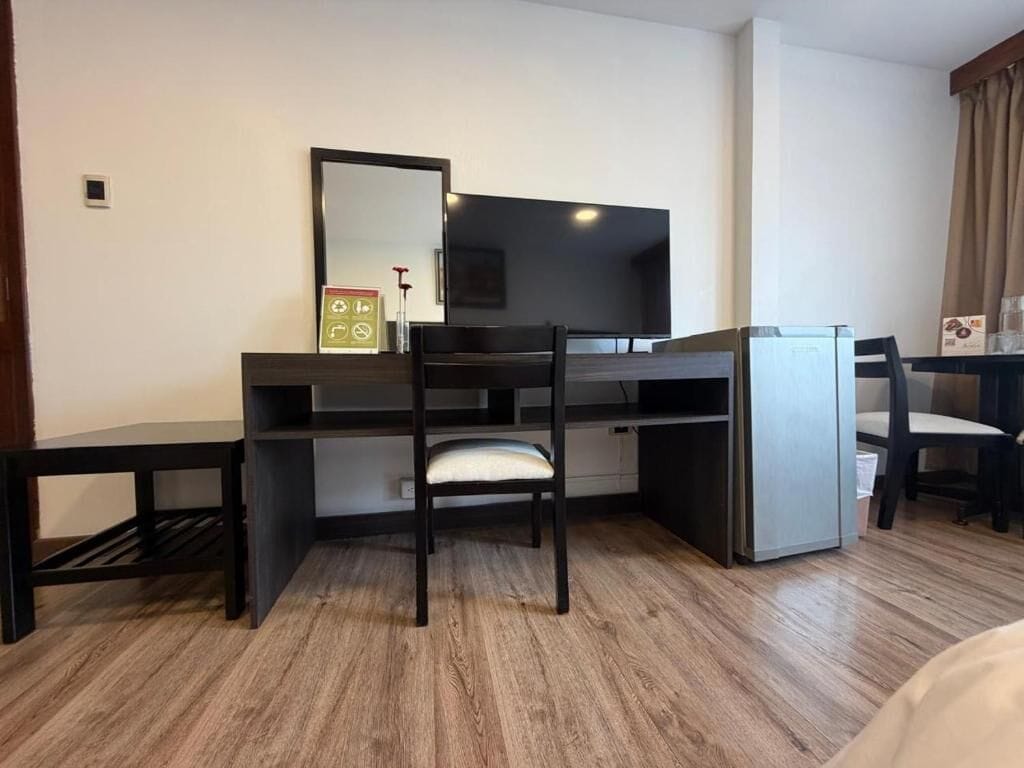 Habitación de hotel con escritorio, silla, televisor y un refrigerador pequeño.