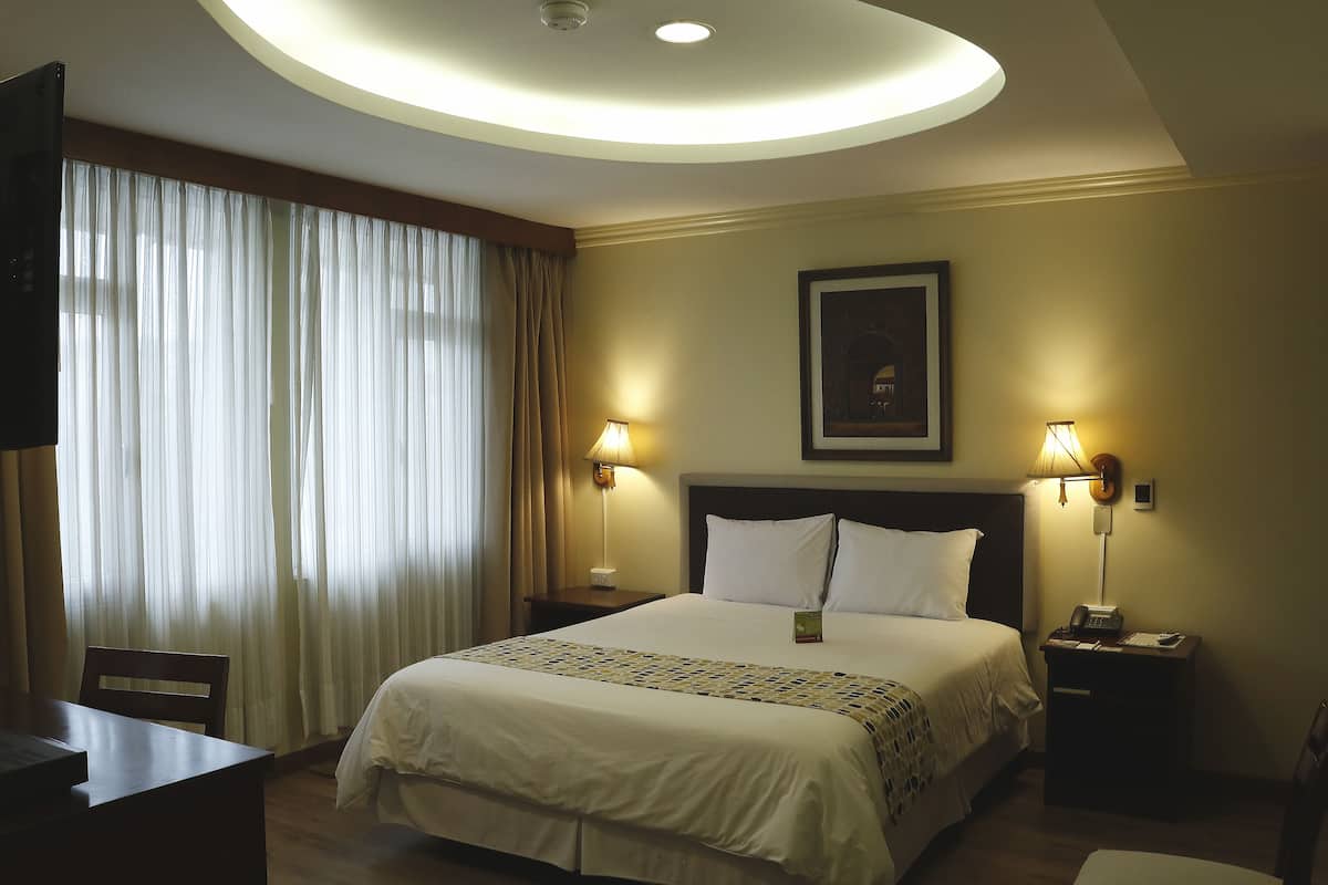 Une chambre d’hôtel avec un lit, deux lampes de chevet, un bureau et une chaise.