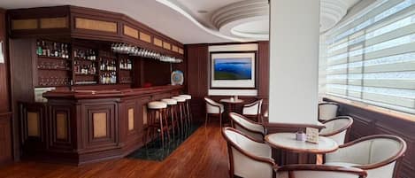 A bar area with a wooden bar counter, stools, and a television screen.
