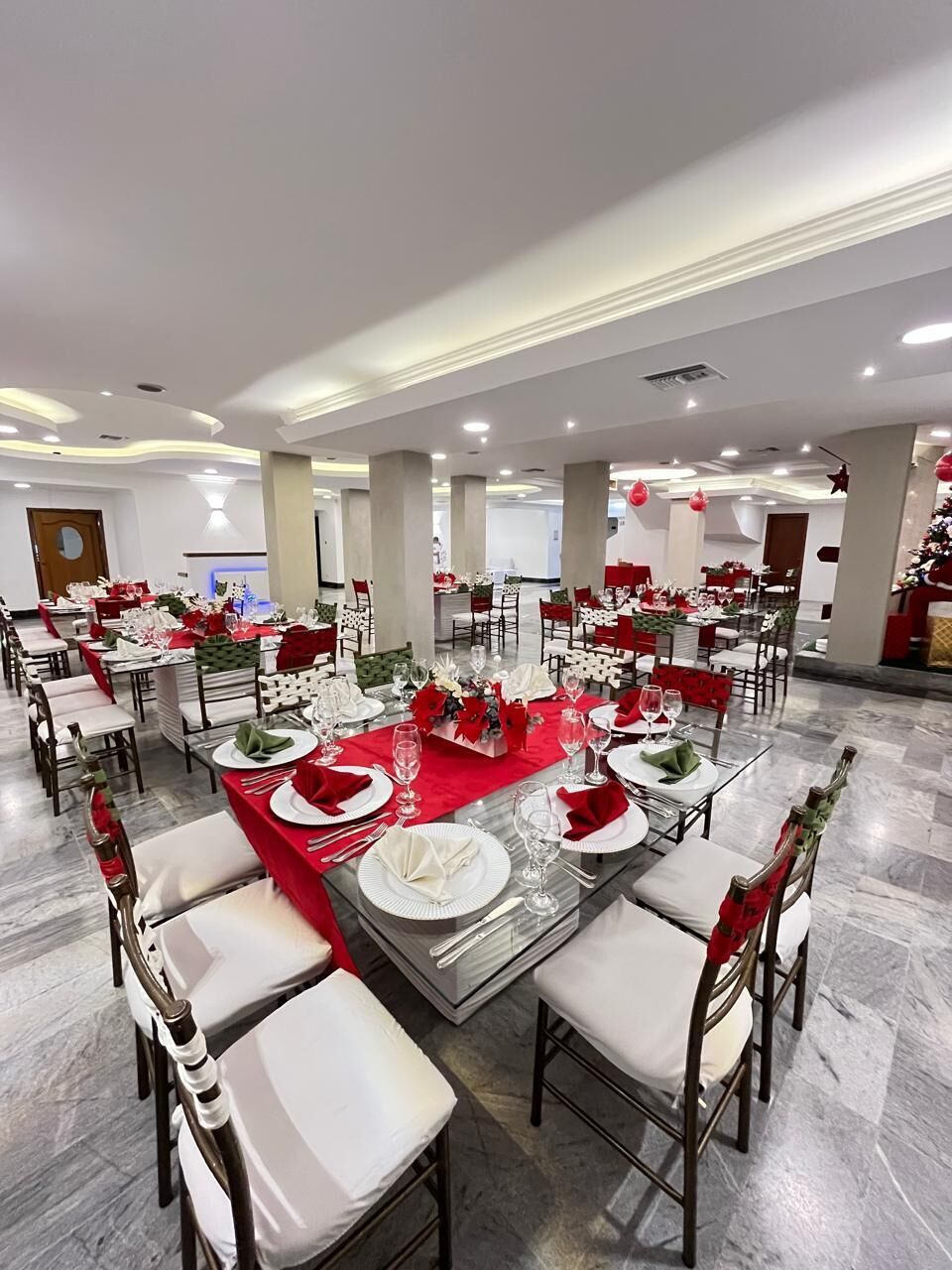 A banquet hall with round tables, white chairs, and red tablecloths.