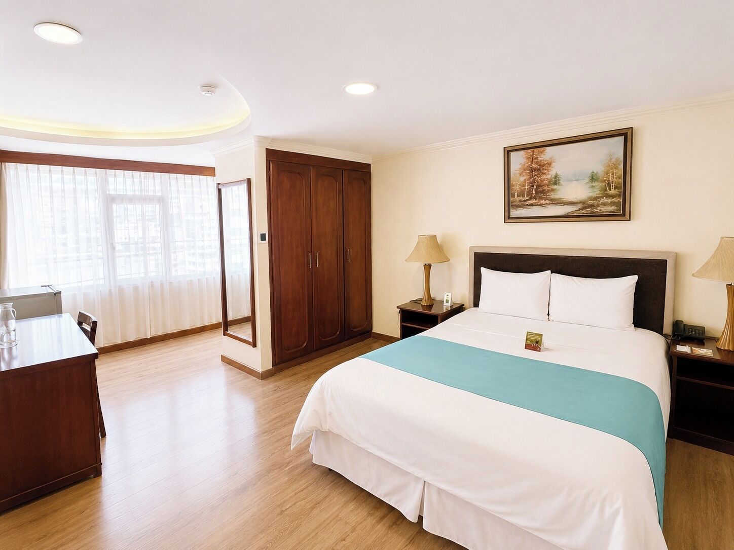 A hotel room with a bed, bedside tables, a wardrobe, a desk, and a window with curtains.