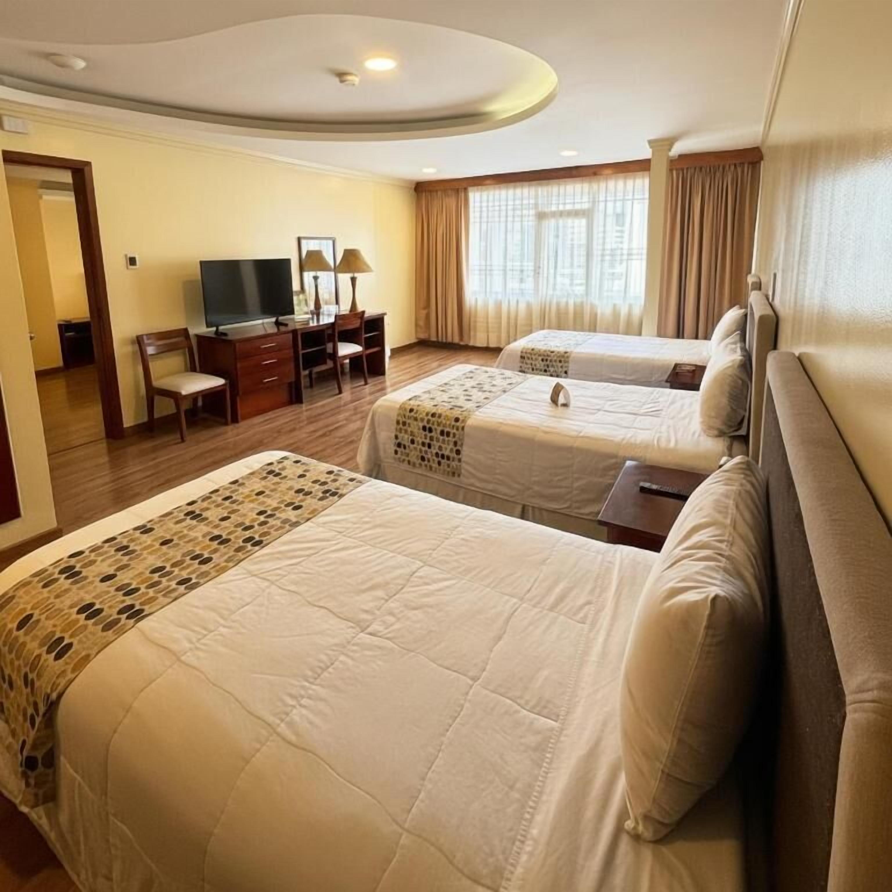 A hotel room with two beds, a desk with a television, and a window with curtains.