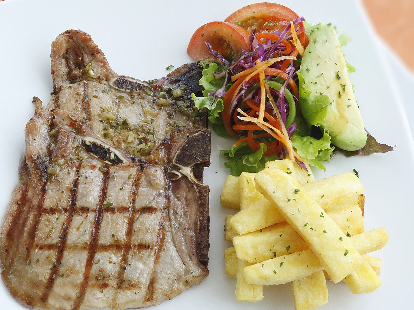 Un plato con carne a la parrilla, ensalada y papas fritas.