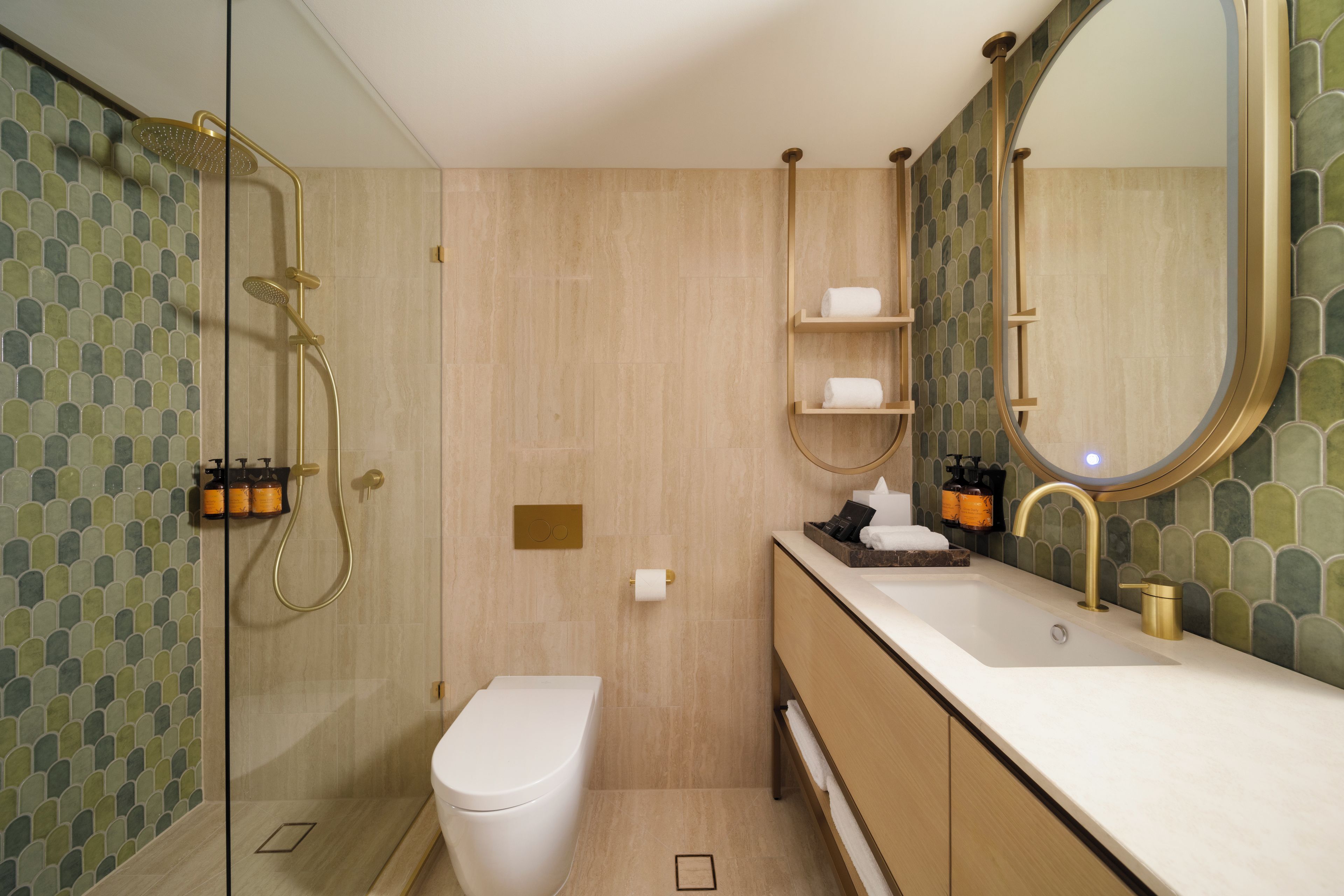 Un baño moderno con ducha envuelta en vidrio, inodoro, lavabo con espejo y estantes con artículos de tocador.