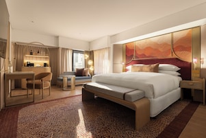 Habitación de hotel con una cama grande, un escritorio, una silla, un sofá y vistas a la ciudad.