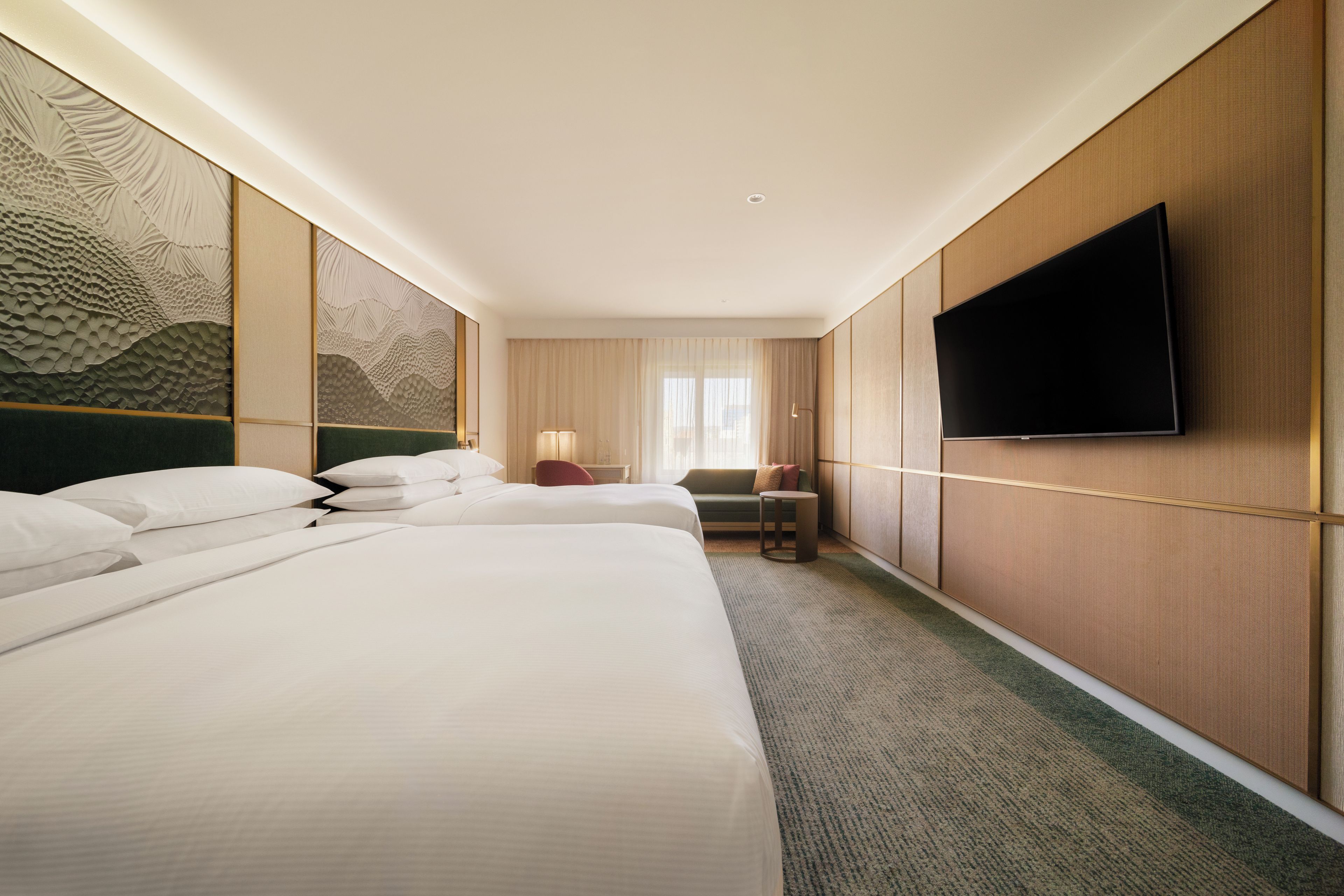 Une chambre d’hôtel avec deux lits, un téléviseur à écran plat fixé au mur et une grande fenêtre avec des rideaux.
