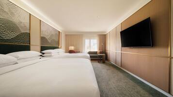 Une chambre d’hôtel avec deux lits, un téléviseur à écran plat fixé au mur et une grande fenêtre avec des rideaux.