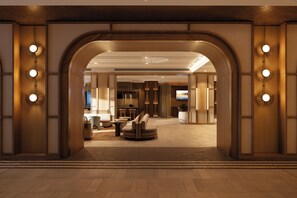 Eine Hotelhalle mit modernem Design, ausgestattet mit einer zentralen Sitzecke, einem Empfangsschalter und einem großen Bildschirm.