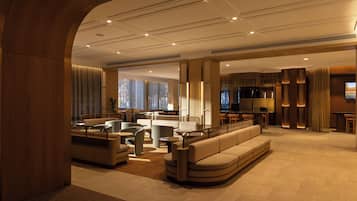 A modern hotel lobby with a seating area, a bar, and a kitchen visible in the background.