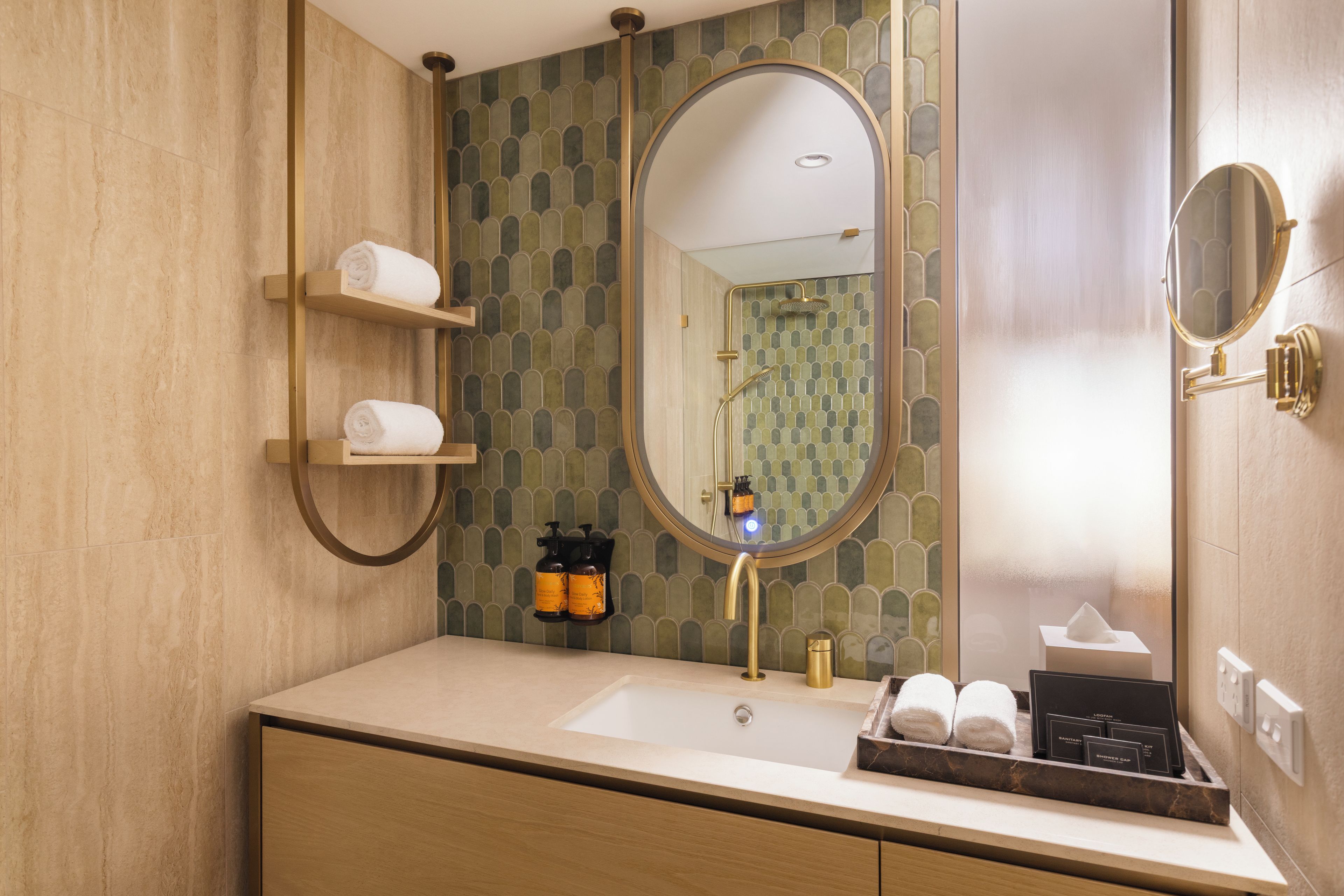 A bathroom with a beige countertop, a round mirror, and a shower area with a tiled wall.