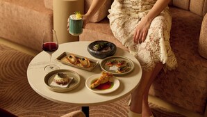 A person seated on a sofa with a table in front of them holding a drink and a small dish. - Amora Hotel Adelaide (Adelaide)