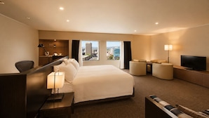 A hotel room with a large bed, a desk with a lamp, a TV, and a view of the city. - Amora Hotel Adelaide (Adelaide)