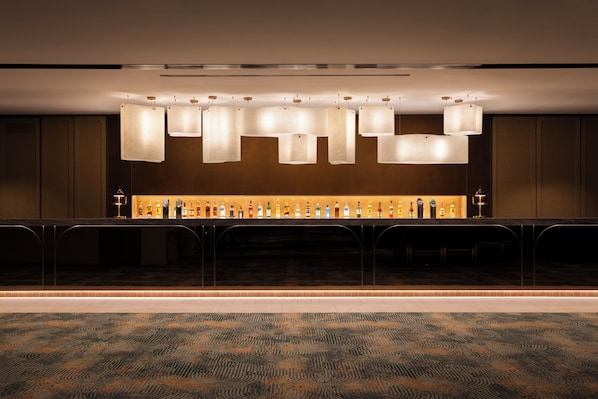 A bar area with a long counter, multiple hanging light fixtures, and a selection of bottles.