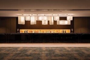 Eine Bar mit einer langen Theke, mehreren hängenden Leuchten und einer Auswahl an Flaschen.