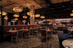 Ein Restaurantinneres mit Sitzecken, Tischen und hängenden Pendelleuchten.