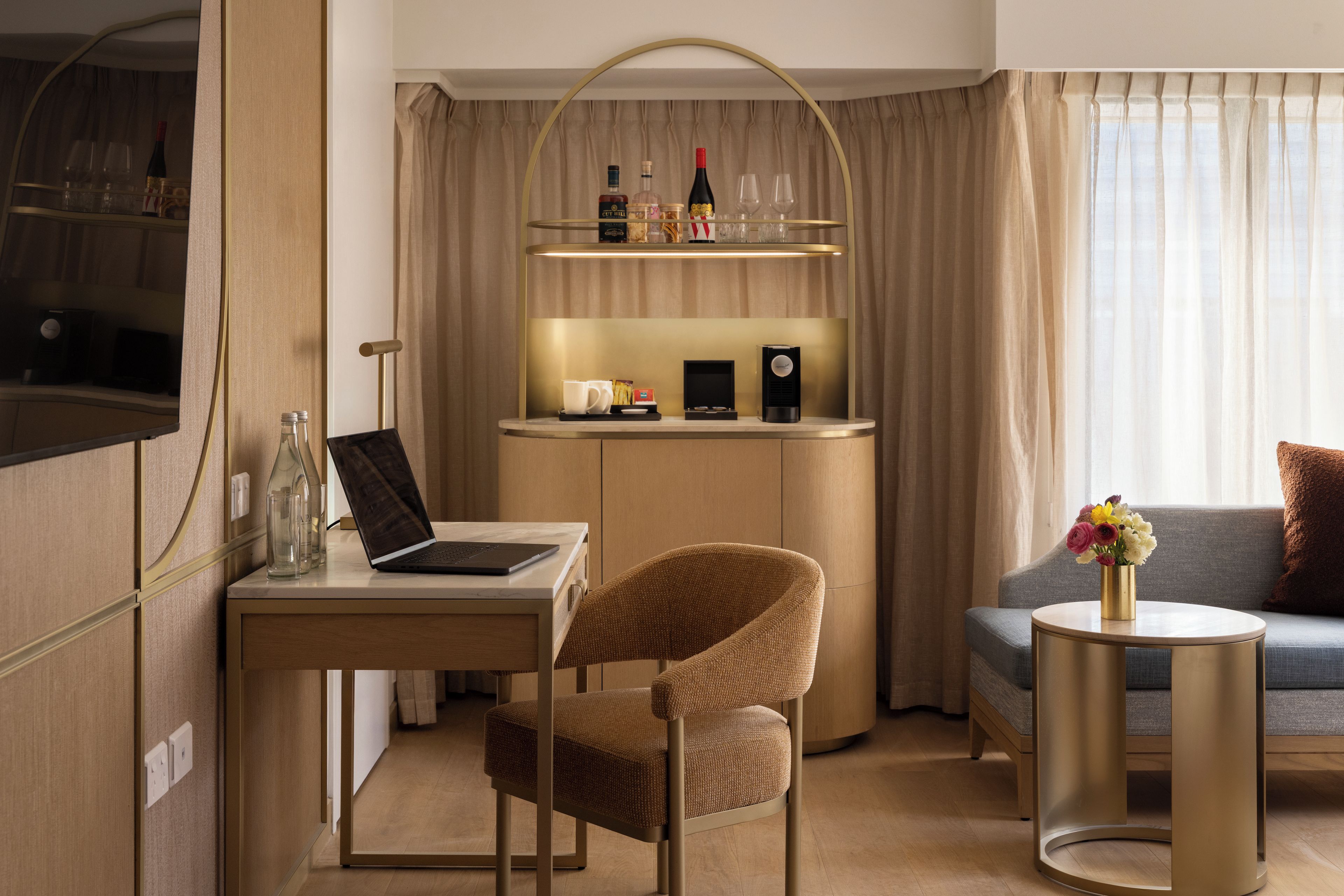 Een moderne hotelkamer met een bureau, laptop, stoel, bank en een klein rond tafeltje met een bloevas.