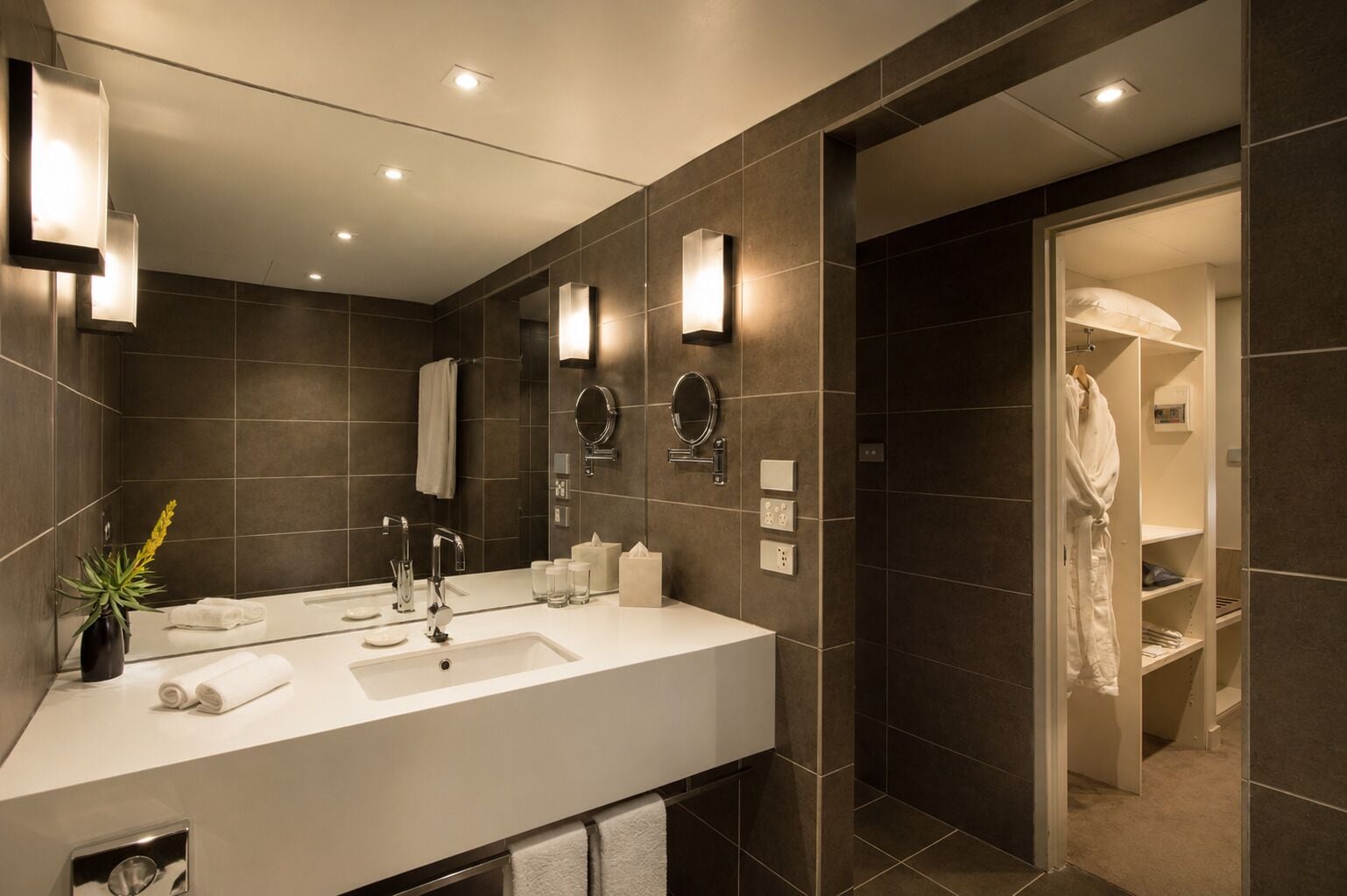 A modern bathroom with a large mirror, dual sinks, and a walk-in shower.