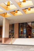 Entrada moderna de un edificio con escaleras, puertas de cristal y un techo con diseños geométricos.
