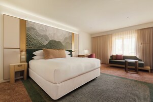 Una habitación de hotel con una cama grande, un sofá, una mesita pequeña y un panel decorativo en la pared.