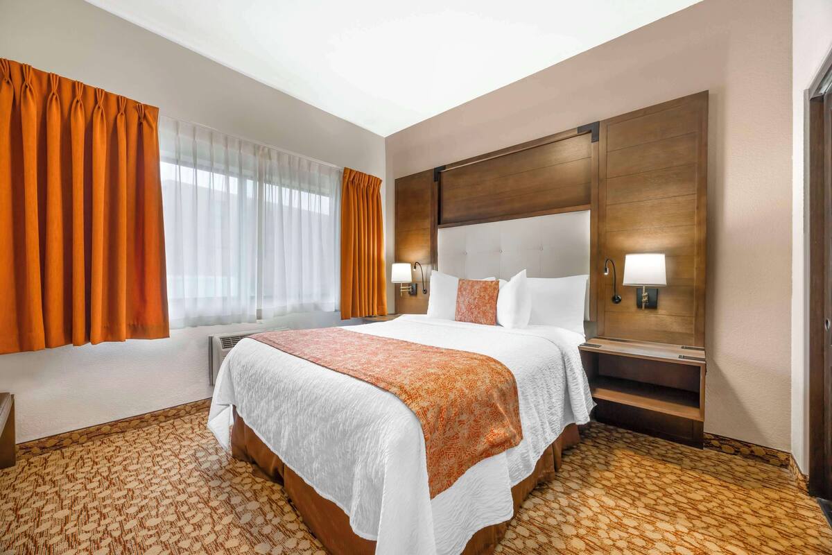 A hotel room with a large bed, a wooden headboard, two bedside lamps, and a patterned carpet.