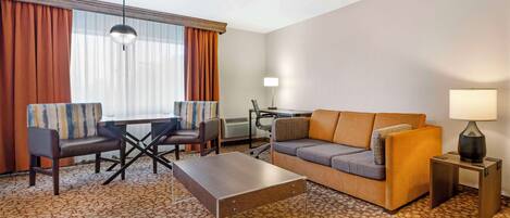 A hotel room with a sofa, two armchairs, a coffee table, a desk, and a lamp.